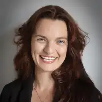 Mujer con cabello castaño oscuro sonriendo, con fondo neutro gris.
