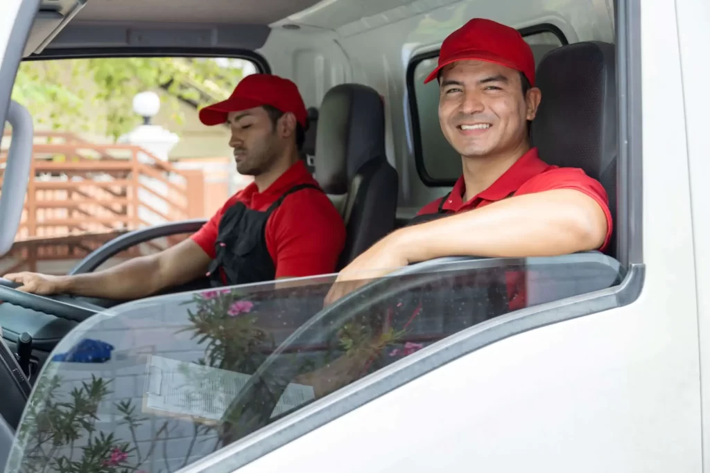 Fotografía de dos conductores de mudanza con uniforme rojo dentro del camión listos para el traslado.